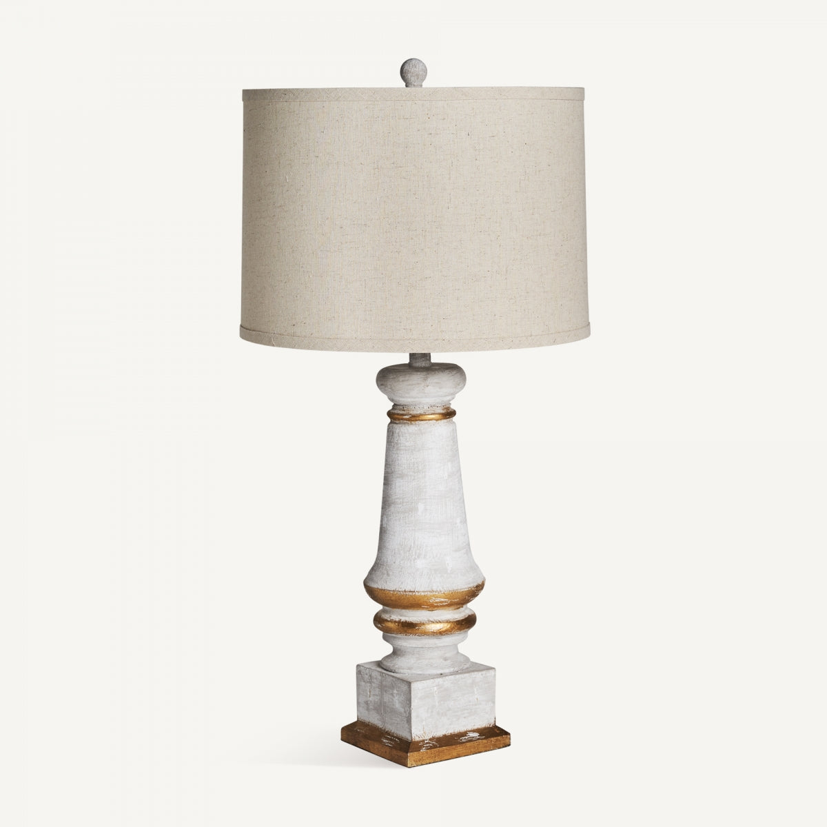 La lámpara de mesa de resina y lino Reg presenta una base decorativa blanca y dorada elaborada con resina y lino, con una pantalla de tambor de tela beige, que ofrece un estilo clásico modernizado sobre un fondo blanco liso.
