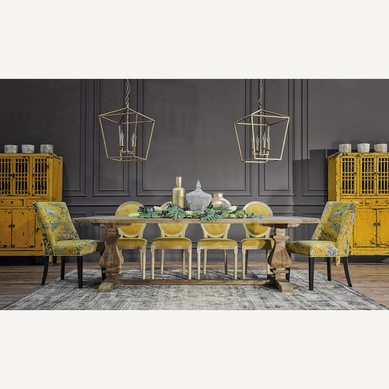 Un comedor con una mesa de madera, sillas con dibujos amarillos, gabinetes amarillos, candelabros con faroles dorados y jarrones en una pared gris se ve bellamente acentuado por la alfombra clásica en viscosa (340x240 cm) Keisi con un diseño vintage.