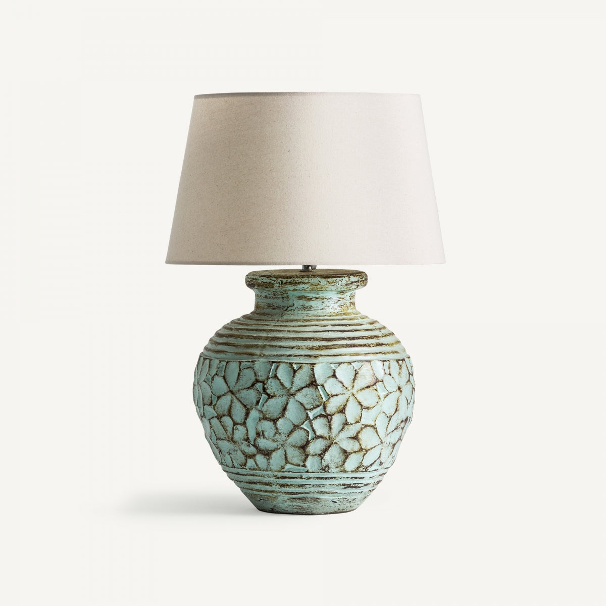 La lámpara de mesa en terracota verde Loto presenta una base de cerámica con un diseño floral texturizado en azul verdoso claro y una sencilla pantalla beige.