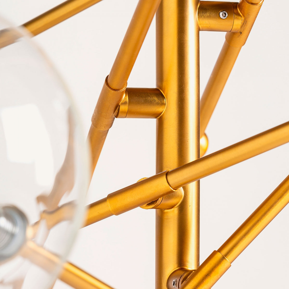 Primer plano de las varillas que se cruzan de la Lámpara colgante en hierro dorado y vidrio S.BOLA, con una bombilla de vidrio transparente en primer plano, destacando la iluminación moderna.