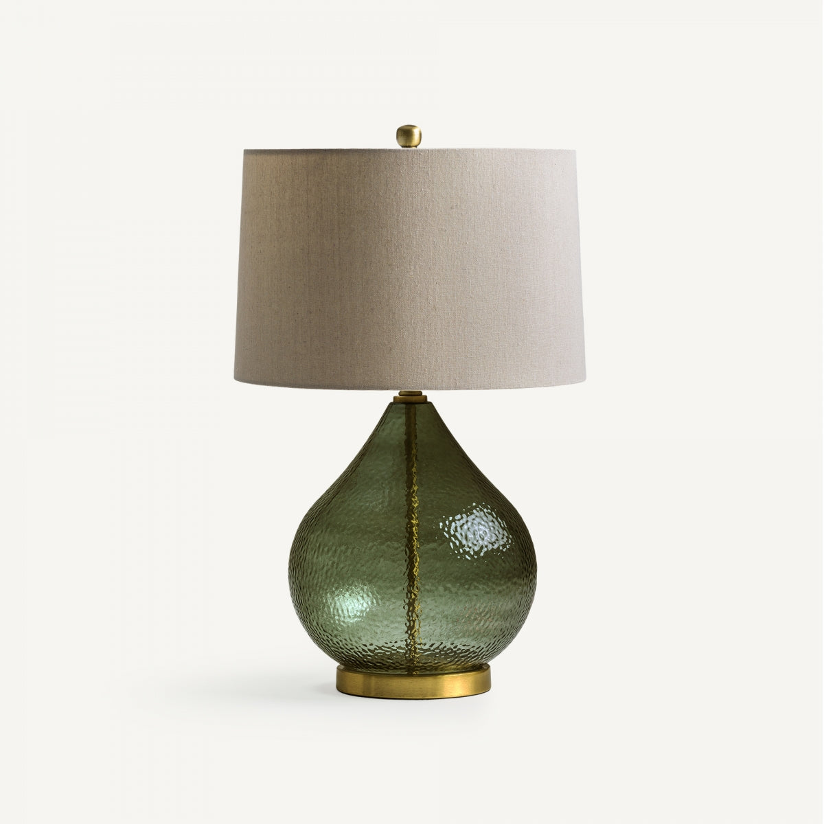 La lámpara de mesa en vidrio verde y metal Lasi destaca por su base texturizada, detalles en latón y pantalla cilíndrica beige, mostrando un diseño elegante sobre un fondo blanco.