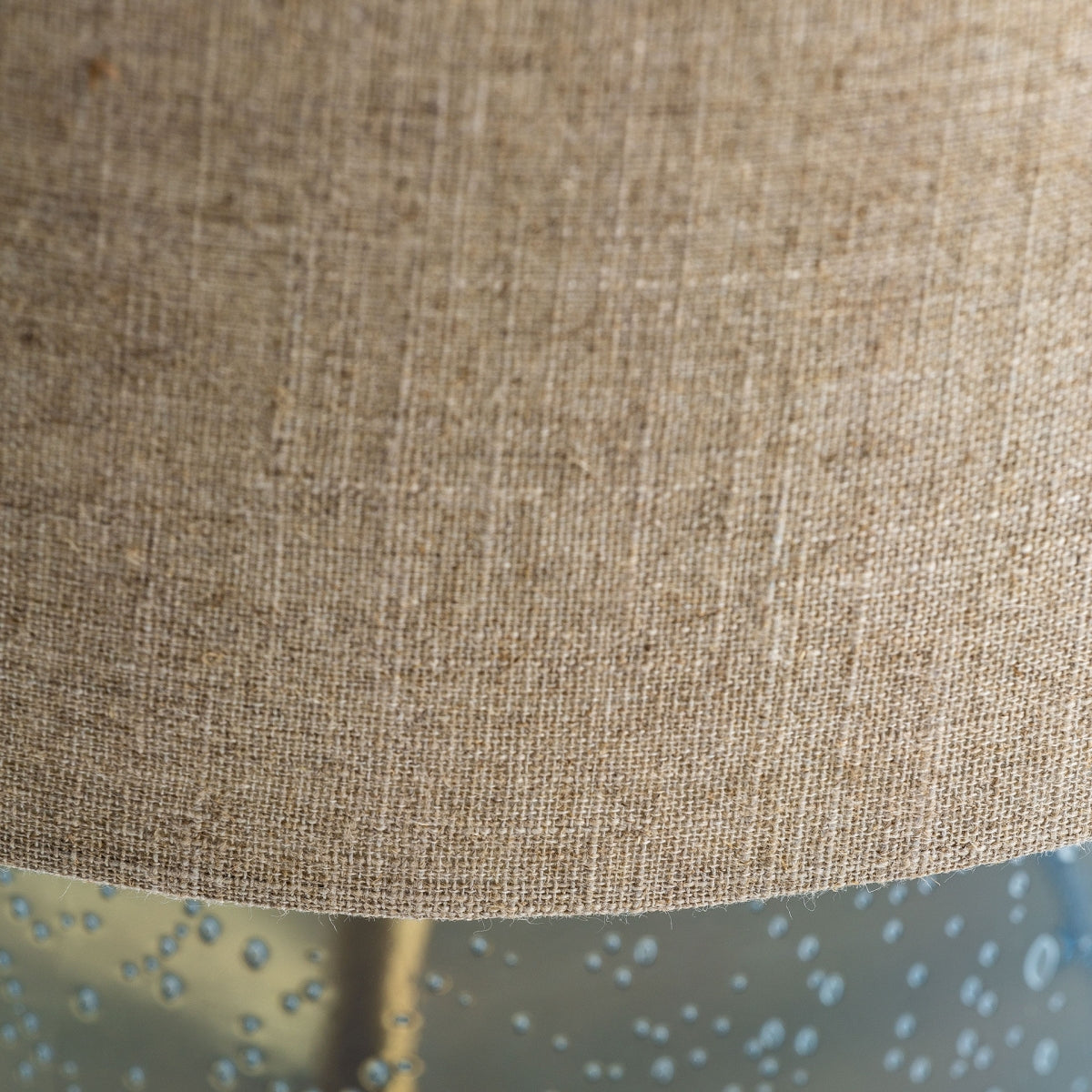 Primer plano de la Lámpara de mesa en vidrio azul y detalles dorados Bluey, que presenta una pantalla beige texturizada y una base azul translúcida con detalles en forma de burbujas, ideal para agregar luz cálida a cualquier espacio.