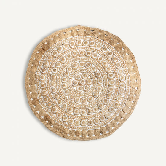 La Alfombra circular en yute y cáñamo (Ø240 cm) Zulai presenta un diseño redondo trenzado en beige y blanco, con anillos concéntricos de patrones geométricos y florales hechos de fibras naturales.