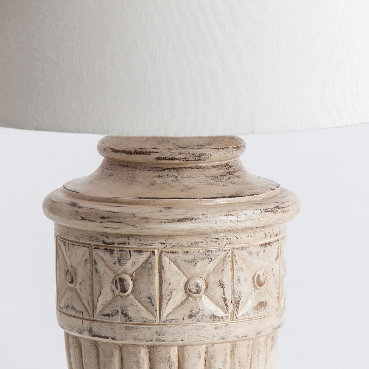 Detalle de la lámpara de sobremesa en madera de mango Hout, que presenta una base tallada de estilo vintage en color beige con un patrón texturizado y pantalla blanca, destacando la auténtica artesanía provenzal.