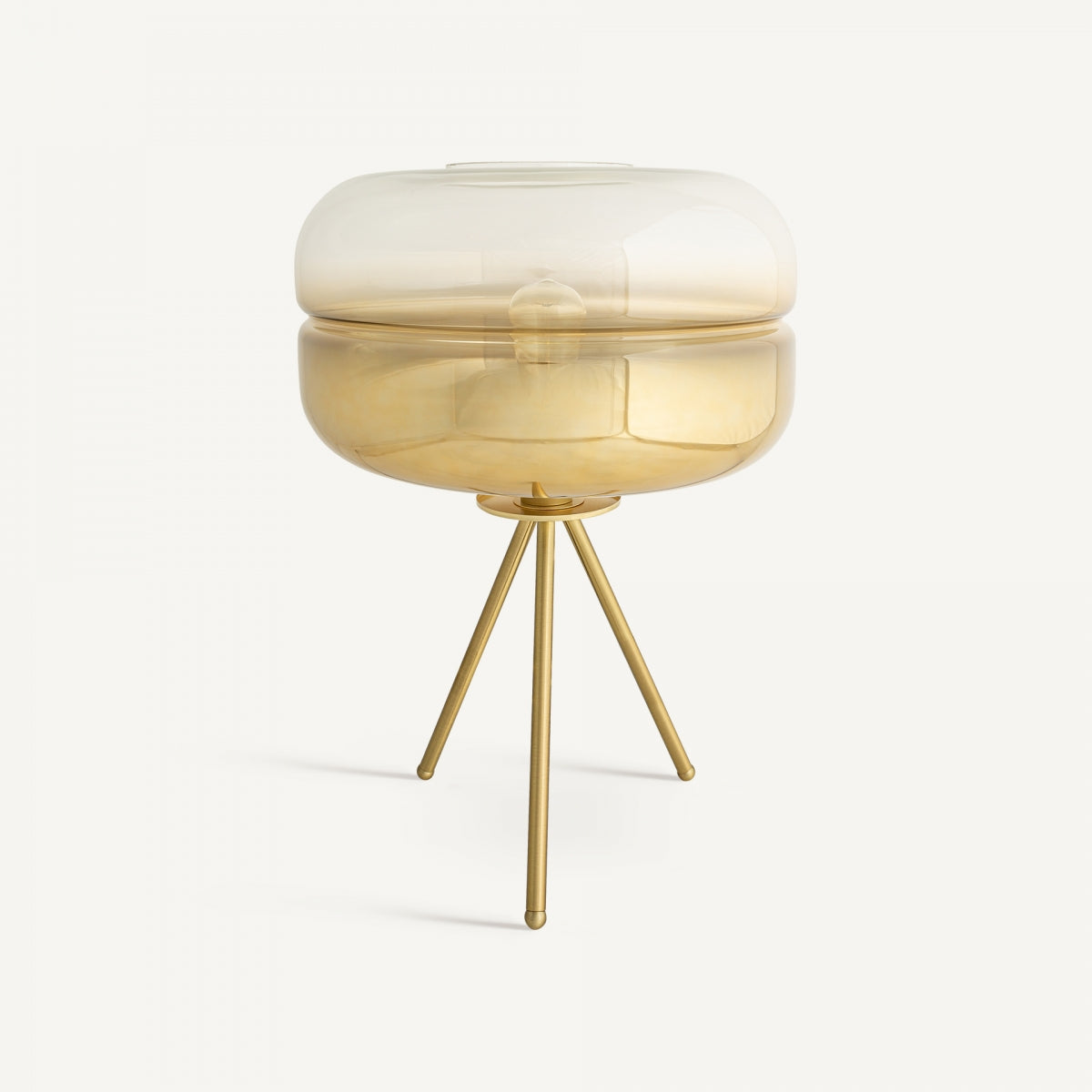La lámpara de mesa en cristal y latón Eyel presenta una pantalla redonda de vidrio ámbar transparente y tres patas doradas en acabado oro degradado, evocando el diseño art déco sobre fondo blanco.