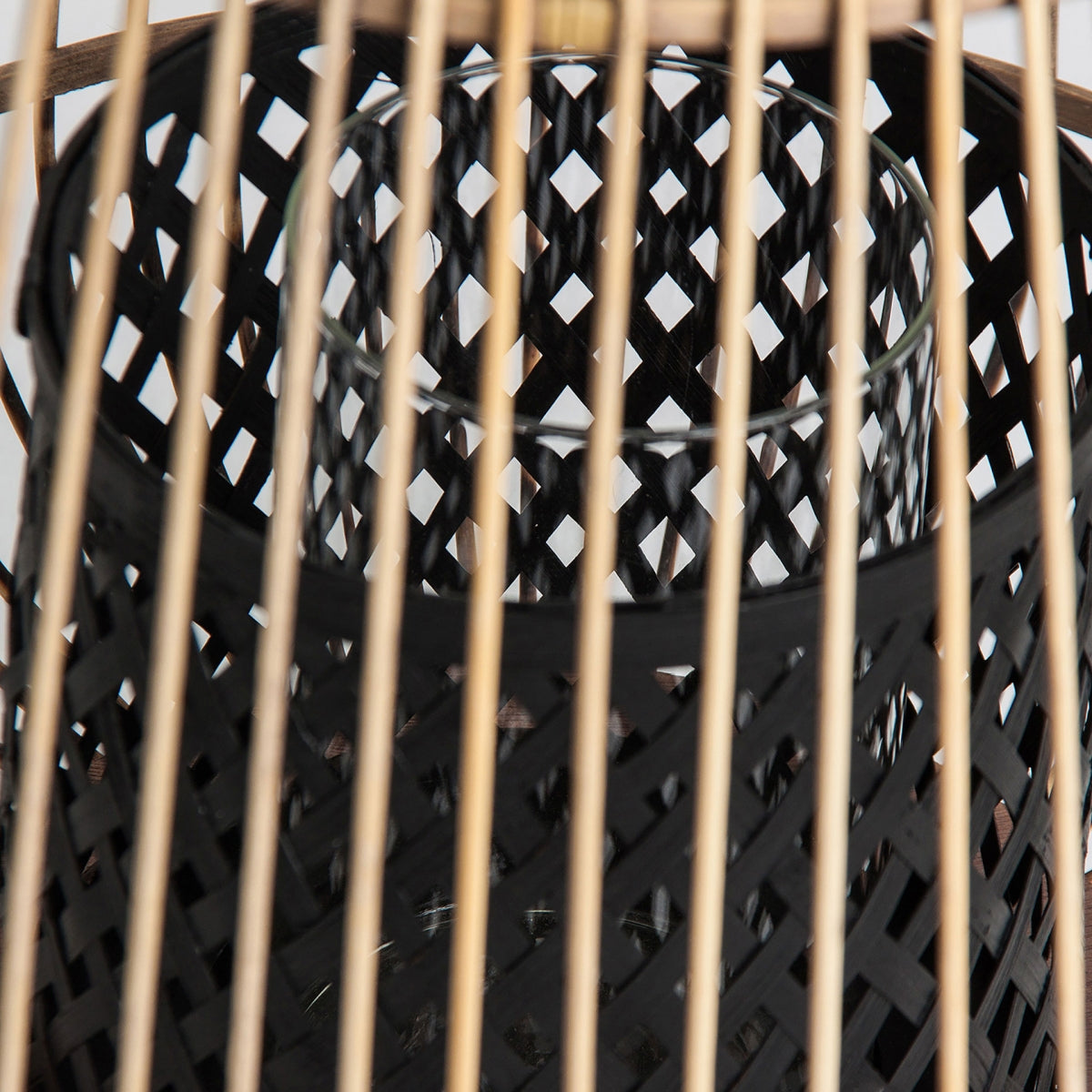 Primer plano de la Portavela de bambú y vidrio Ghia, que presenta una estructura de bambú negro tejido que encierra una linterna de metal negro con patrón de celosía y un soporte de vidrio interior.