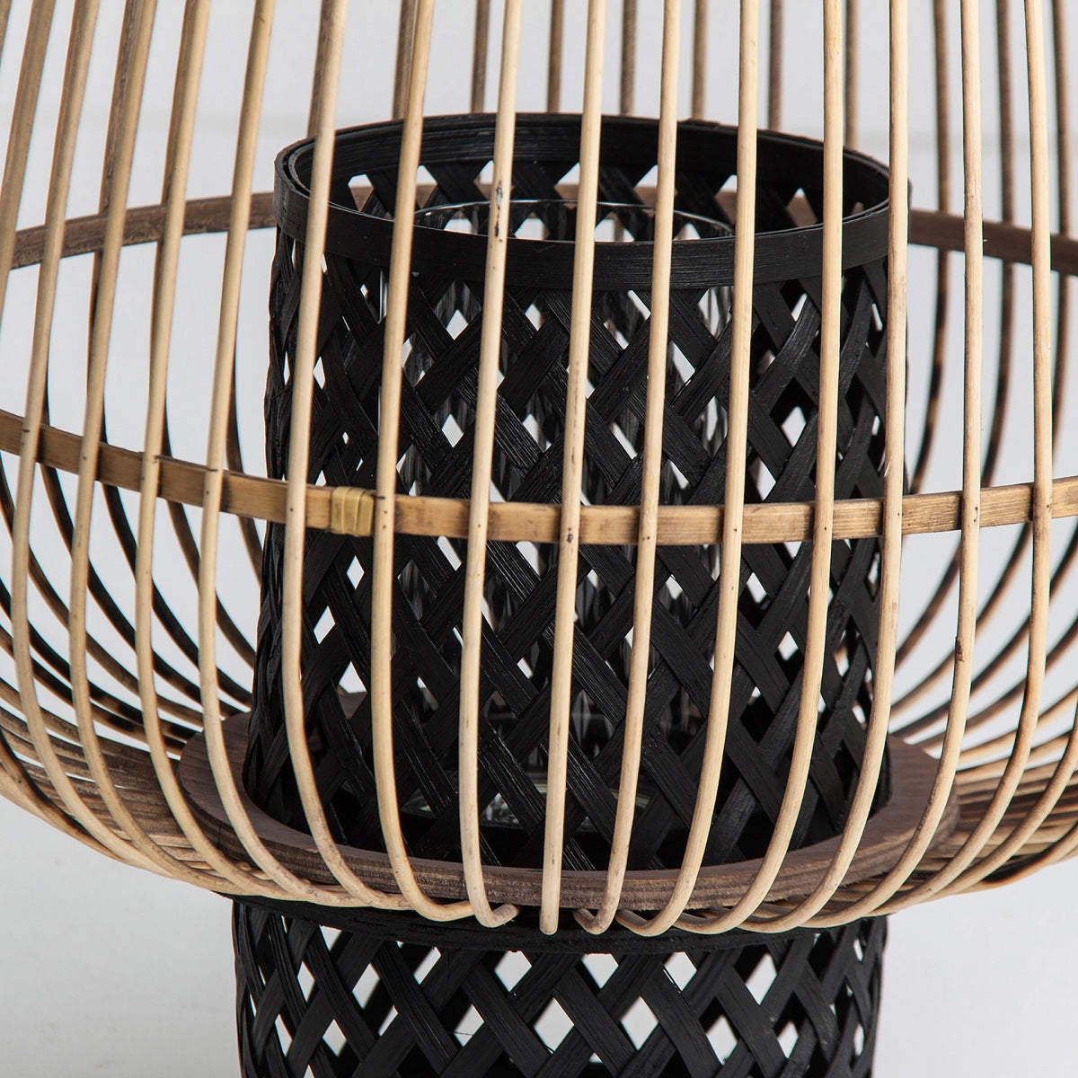 Este primer plano muestra el Portavelas moderno de bambú y ratán Ghiare, que presenta una cesta negra tejida dentro de una estructura de madera calada. Sus líneas elegantes y tonos cálidos realzan cualquier decoración cálida, representando un estilo contemporáneo.