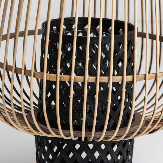 Este primer plano muestra el Portavelas moderno de bambú y ratán Ghiare, que presenta una cesta negra tejida dentro de una estructura de madera calada. Sus líneas elegantes y tonos cálidos realzan cualquier decoración cálida, representando un estilo contemporáneo.
