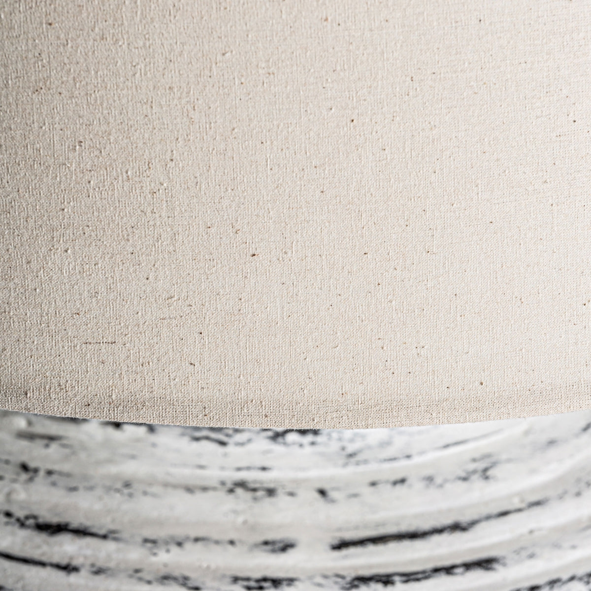 Primer plano de la Lámpara de sobremesa en terracota blanca Coria, con pantalla de tela beige y base de cerámica texturizada con líneas blancas y negras, ideal para agregar encanto shabby chic a su espacio.
