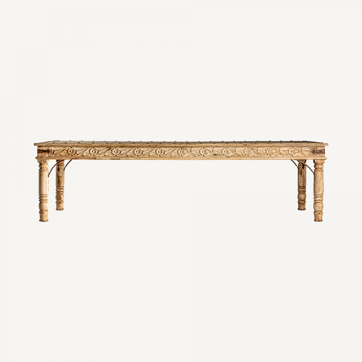 Una gran mesa de comedor de madera de mango llamada "Mesa de comedor grande en madera de mango Kalyan", con un exquisito diseño artesanal y tallados intrincados en las patas y los lados, se encuentra sobre un fondo blanco liso.