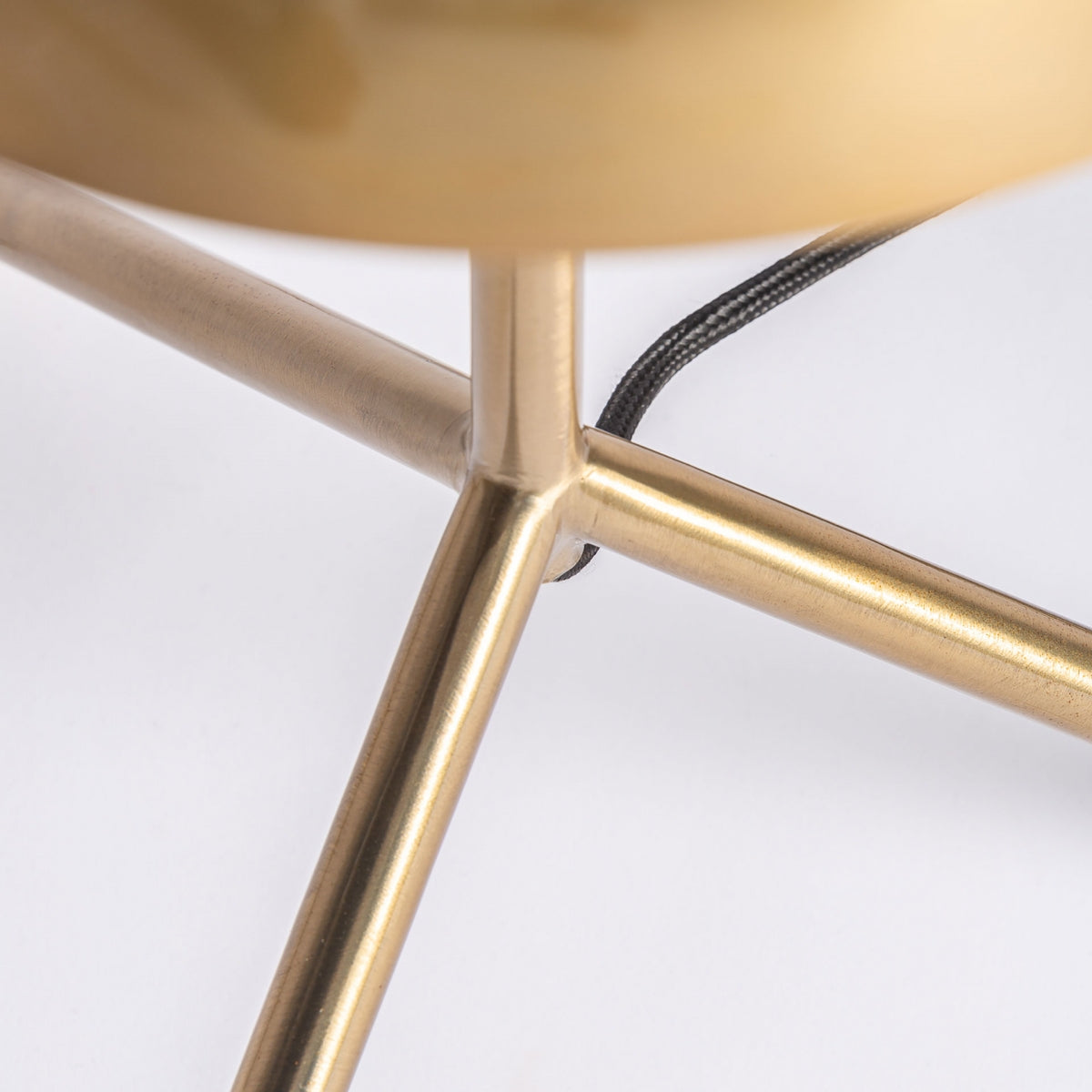 Primer plano de las varillas de hierro dorado entrecruzadas de la lámpara de sobremesa en hierro dorado Kelheim con un cable negro, sobre un fondo blanco, resaltando su elegante diseño art déco.
