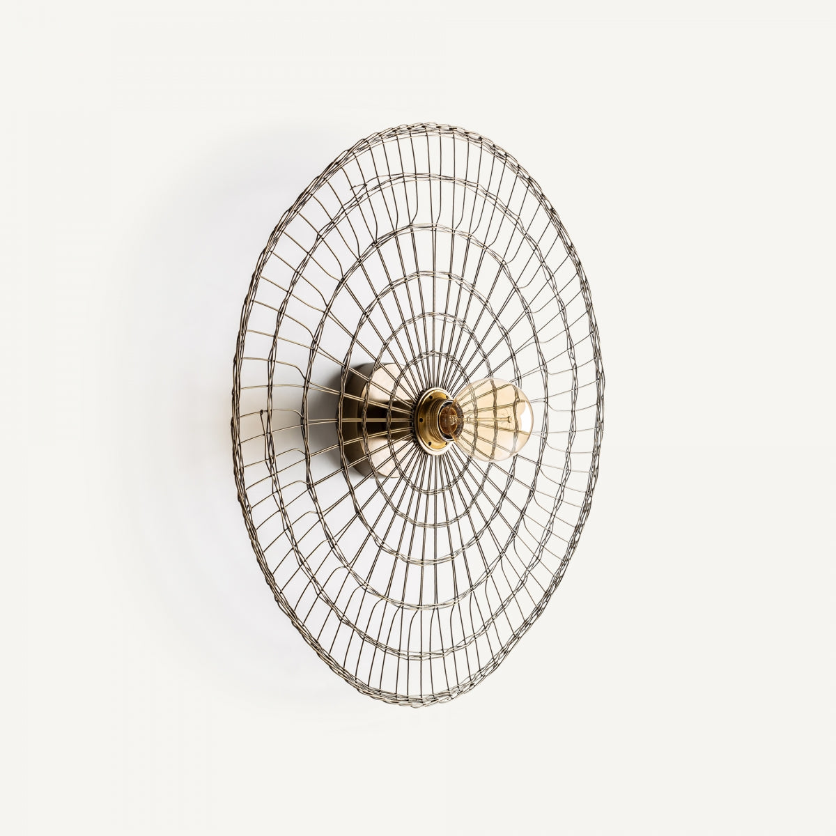 El Aplique de pared en hierro color oro Korum es un ventilador eléctrico de pared con diseño industrial y jaula de seguridad de alambre de metal, mostrado de frente sobre un fondo blanco.