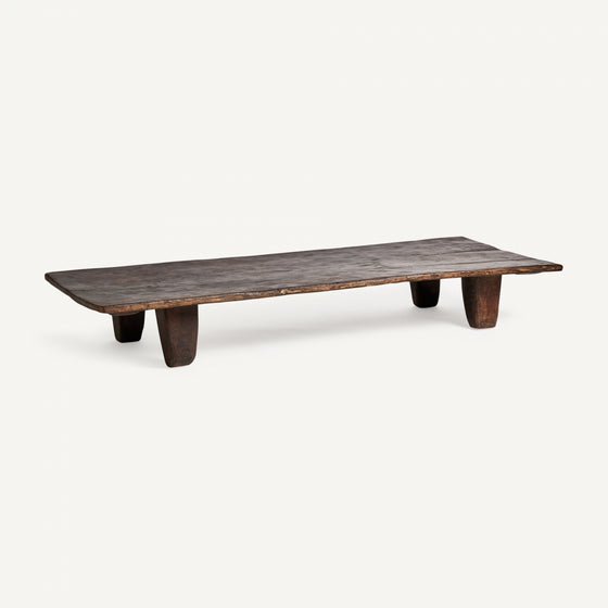 La Mesa de centro rectangular en madera de teka Erara es un banco bajo y rectangular de madera elaborado en teca maciza, que presenta una superficie plana y cuatro patas cortas sobre un fondo blanco prístino, resaltando su diseño artesanal.