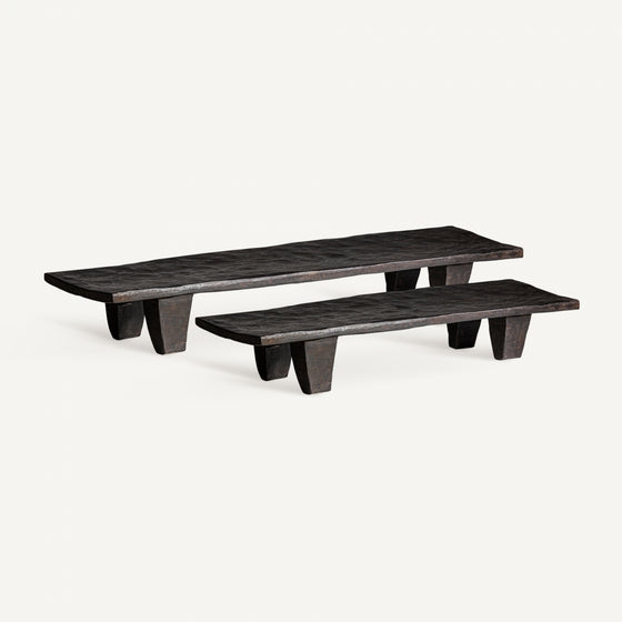 Dos bancos elaborados en madera de teca, con longitudes variadas, tapas planas y patas rectangulares resistentes con un exquisito diseño artesanal, se ubican sobre un fondo liso.