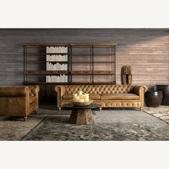 Un sofá y un sillón de cuero se ubican frente a una estantería; la Alfombra clásica en viscosa (300x200 cm) Ewa agrega elegancia y comodidad, complementada por una mesa de café con velas y una decoración texturizada para un espacio acogedor.