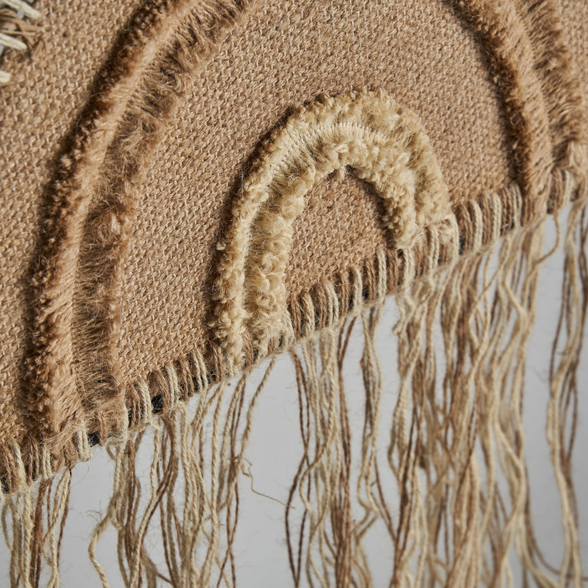Primer plano del Panel decorativo de yute y hierro Whil, un colgante de pared de estilo boho con patrones arqueados y largos flecos de yute beige, que aporta calidez y textura natural a cualquier espacio.