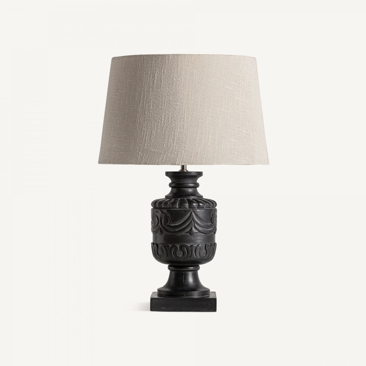 La Lámpara de sobremesa en madera de mango y algodón Gance destaca con su base tallada negra y pantalla de tejido beige, ideal para aportar una iluminación acogedora sobre fondo blanco.