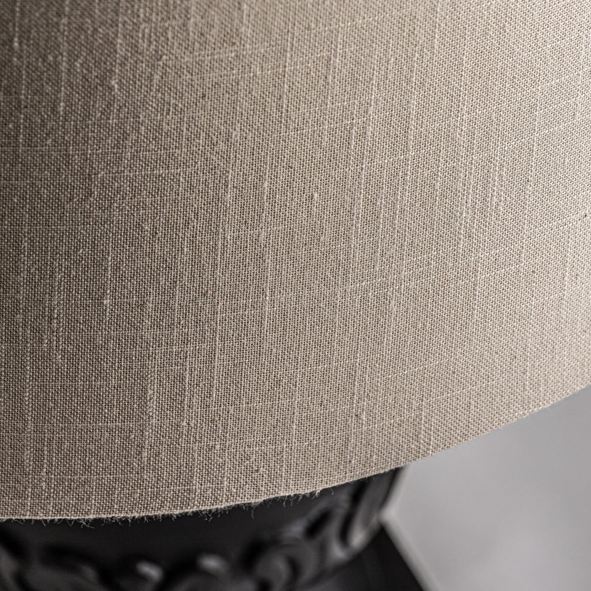Primer plano de la Lámpara de sobremesa en madera de mango y algodón Gance, que presenta una pantalla de algodón texturizado beige que cubre parcialmente una base decorativa de madera de mango negra, ideal para crear una iluminación cálida y acogedora.
