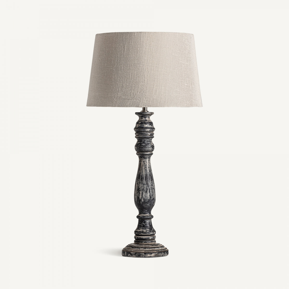 La lámpara de mesa en madera de mango Larza presenta una base de madera oscura envejecida y una pantalla de tela beige, elaborada con materiales de primera calidad y mostrada sobre un fondo blanco liso.