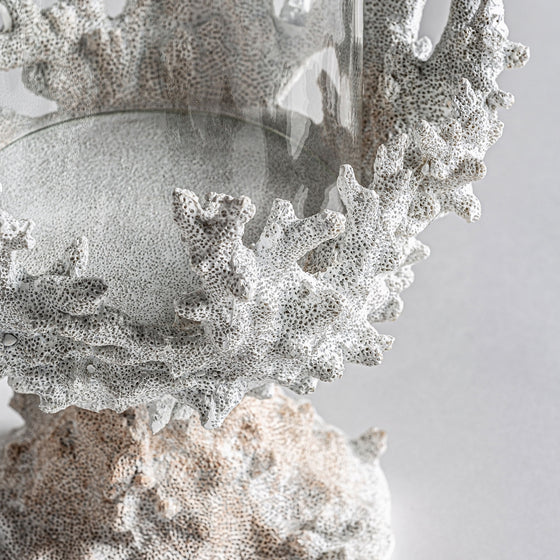 El Portavelas de resina blanca Arrecife G es un cuenco de vidrio transparente con una estructura texturizada de color blanco coral. Su intrincado diseño de inspiración nórdica y su base a juego crean una decoración sofisticada y elegante sobre un fondo neutro.