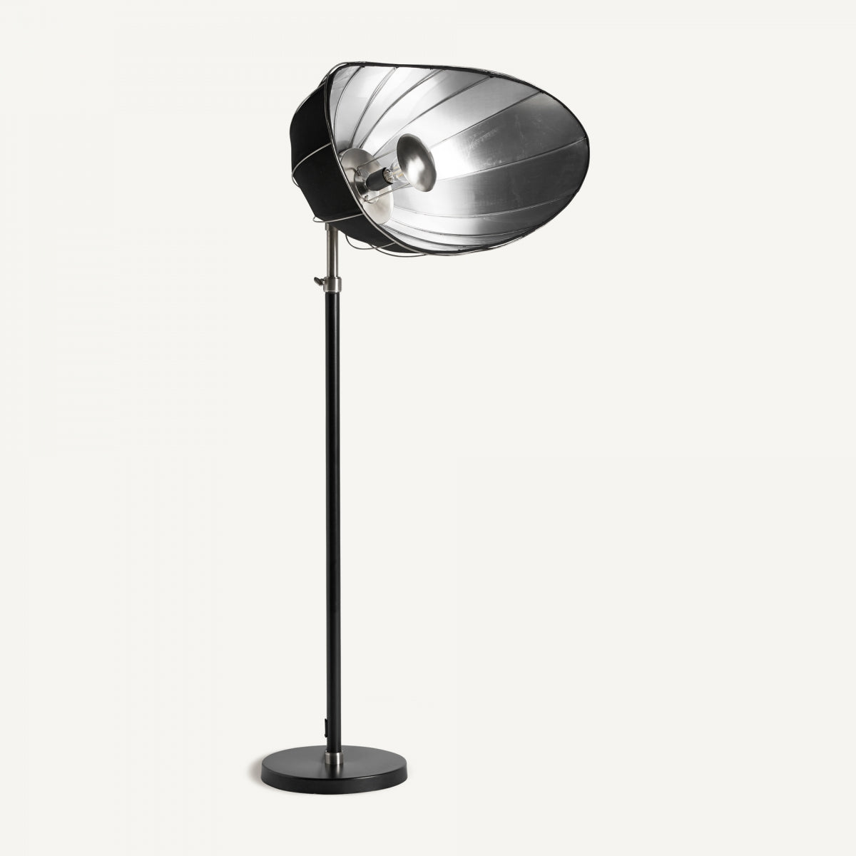 La Lámpara de pie en hierro elevable Alia S es alta, negra, con reflector metálico redondo y bombilla expuesta sobre base circular; presenta iluminación ajustable para luz versátil contra un fondo blanco.