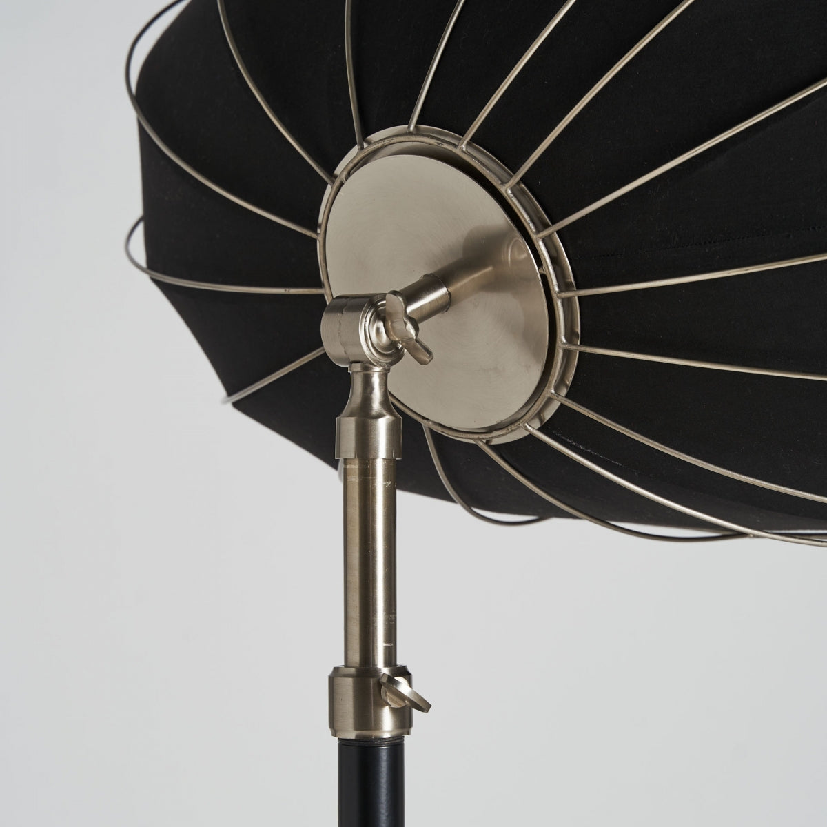 Primer plano de la parte trasera de la Lámpara de pie en hierro elevable Alia S, que presenta una pantalla de tela negra, estructura de metal y brazo orientable para iluminación, añadiendo un toque elegante sobre un fondo liso.