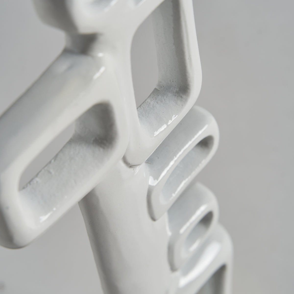 Primer plano de la Figura decorativa de aluminio blanco y dorado Hubble, que presenta bucles rectangulares brillantes e interconectados sobre un fondo liso, perfecto para quienes aprecian el diseño contemporáneo.