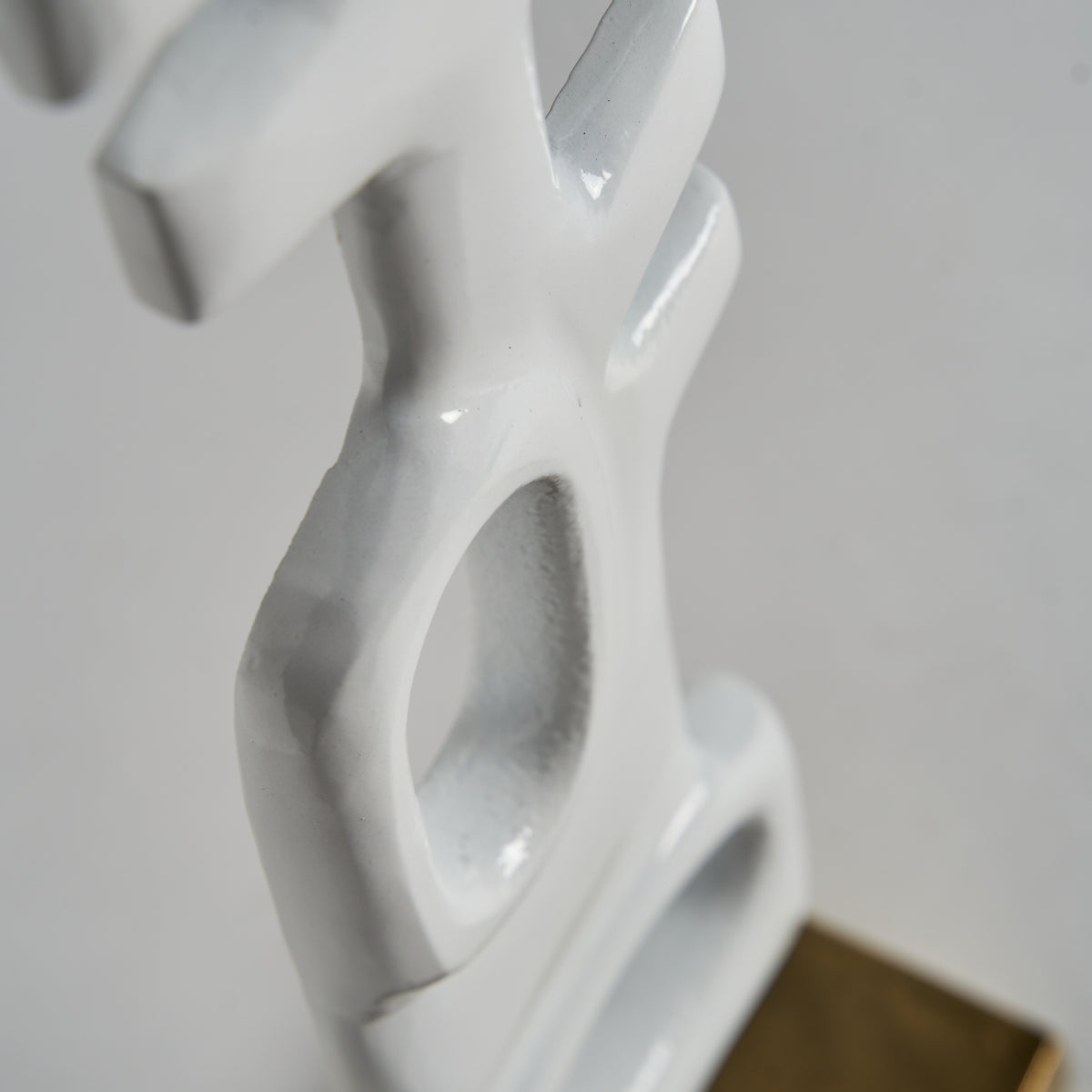 Primer plano de la Figura decorativa de aluminio blanco y dorado Hubble S, una escultura abstracta con superficies lisas y angulares, recorte de forma ovalada y base de color marrón claro; una pieza que irradia elegancia y modernidad.