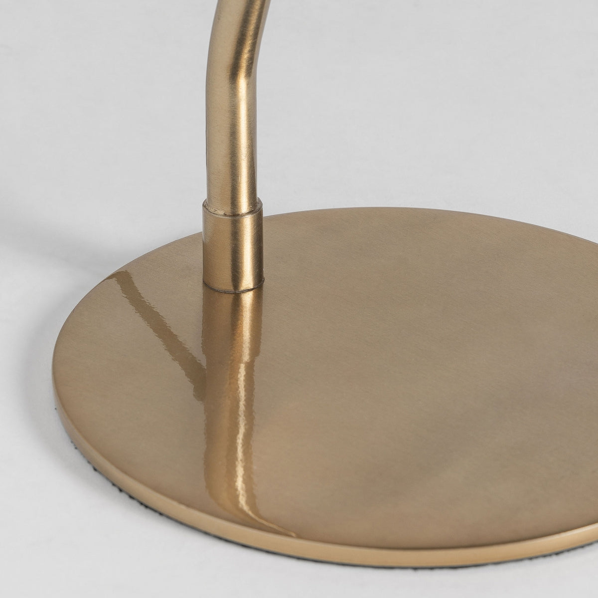 Un primer plano de la Lámpara de mesa en hierro oro y negro Tresa muestra su base metálica y su tallo curvo en oro cepillado, encarnando una iluminación elegante y añadiendo un toque de estilo art déco sobre un fondo sencillo.