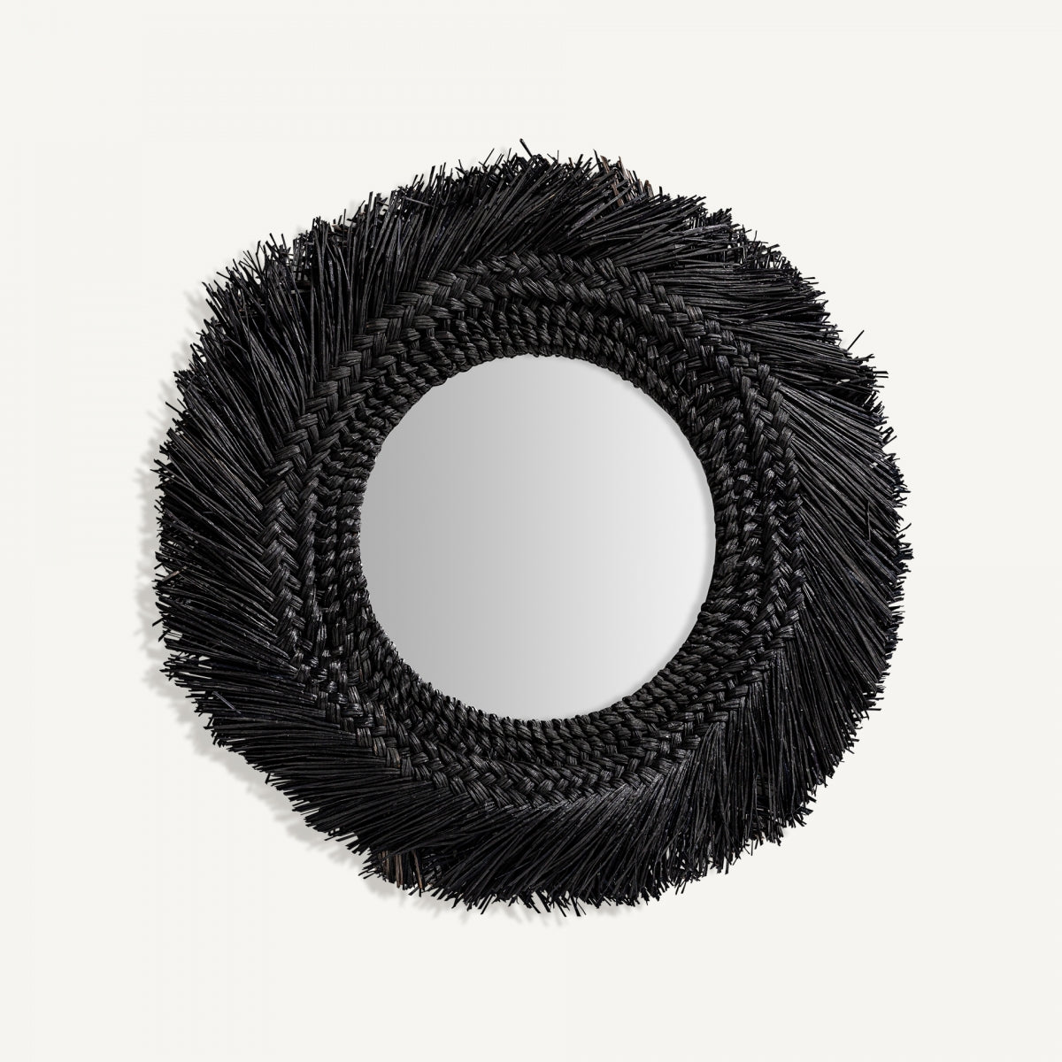 El Espejo redondo en fibra natural (70x70 cm) Desouk tiene marco negro texturizado y bordes con flecos, perfecto para añadir un toque contemporáneo sobre fondo blanco liso.