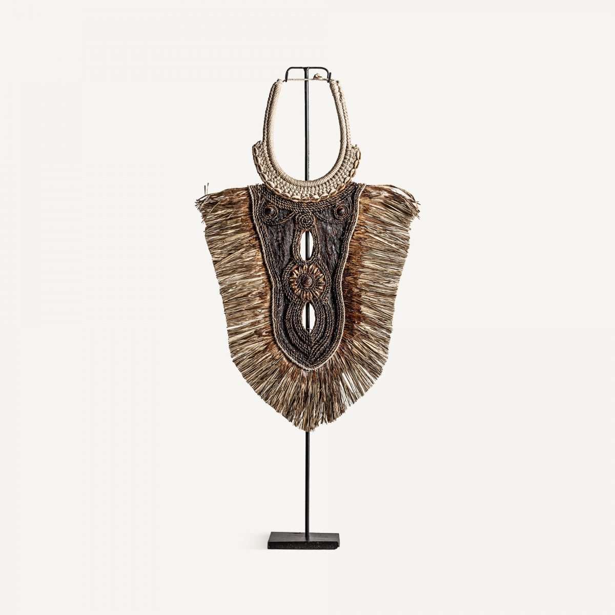La Figura decorativa en fibra natural Sira, con detalles artesanales y flecos de fibras naturales, perfecta para estilo étnico y decoración artesanal, se exhibe sobre un soporte negro frente a un fondo blanco.