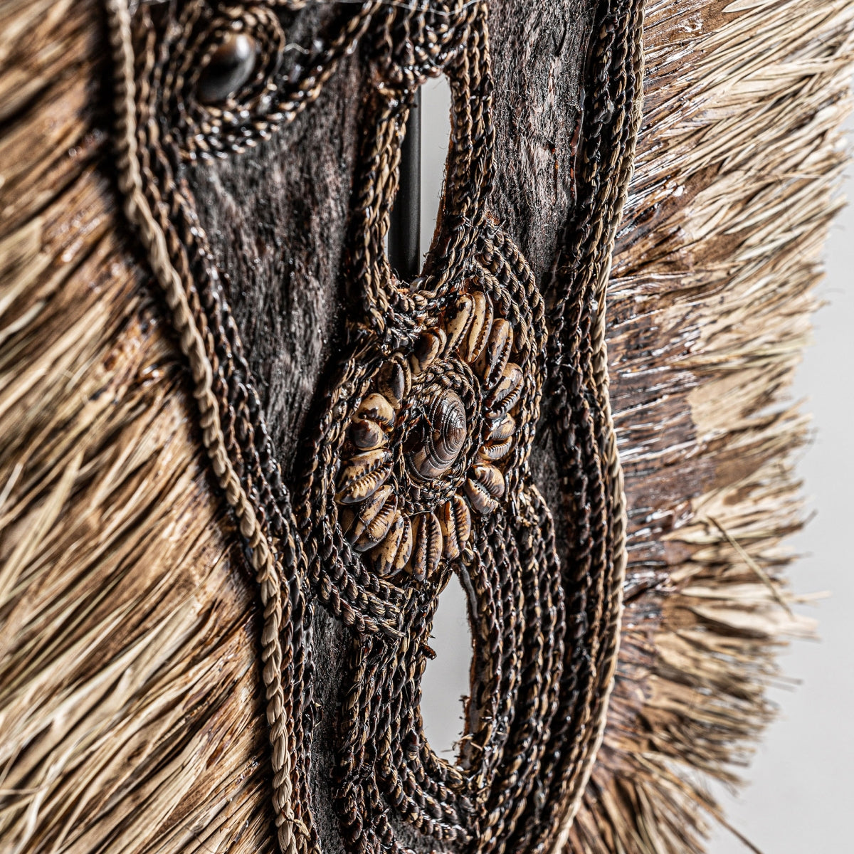 Primer plano de la figura decorativa en fibra natural Sira, que muestra fibras tejidas, cuerda trenzada y conchas decorativas en un diseño circular sobre madera texturizada, perfecto para decoración artesanal.