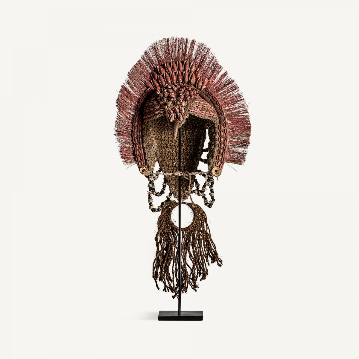 Figura decorativa en fibra natural étnica Kasai: pieza de diseño étnico con penacho alto en abanico, elementos tejidos, cuentas colgantes y flecos sobre base negra, destacando como figura decorativa contra un fondo blanco.