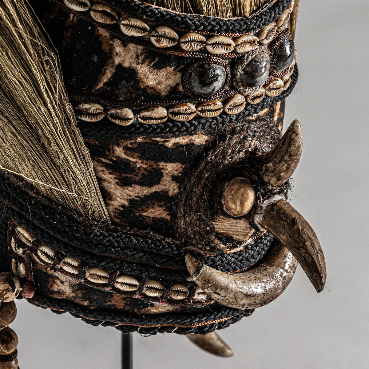 Primer plano de la máscara de figura decorativa en fibra natural, con tela con estampado animal, conchas cauri, cuerda, garras de animales y fibra natural para un toque de artesanía auténtica.