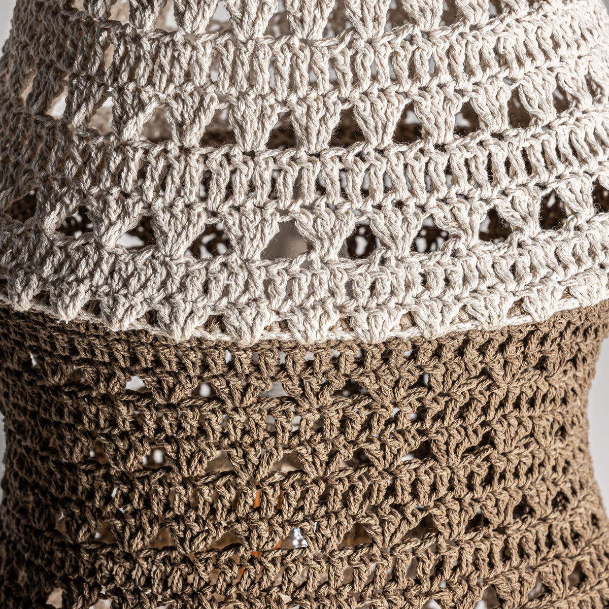 Primer plano de la lámpara colgante Kiran, confeccionada con un tejido de hilos marrones y blancos con un detallado patrón de crochet. Los intrincados bucles y texturas evocan un estilo étnico, capturando con belleza la esencia de la artesanía del algodón natural.