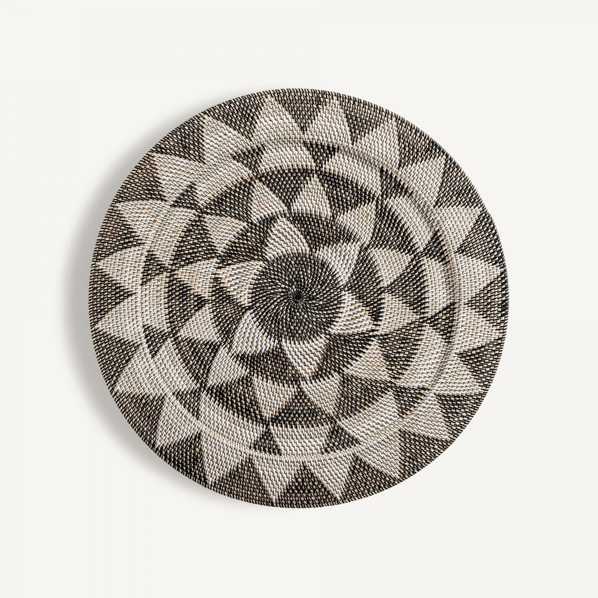 Una canasta de ratán redonda y plana con patrones geométricos de estrellas en blanco y negro—Panel decorativo en ratán con estilo étnico Zirba—exhibida elegantemente sobre un fondo blanco liso.