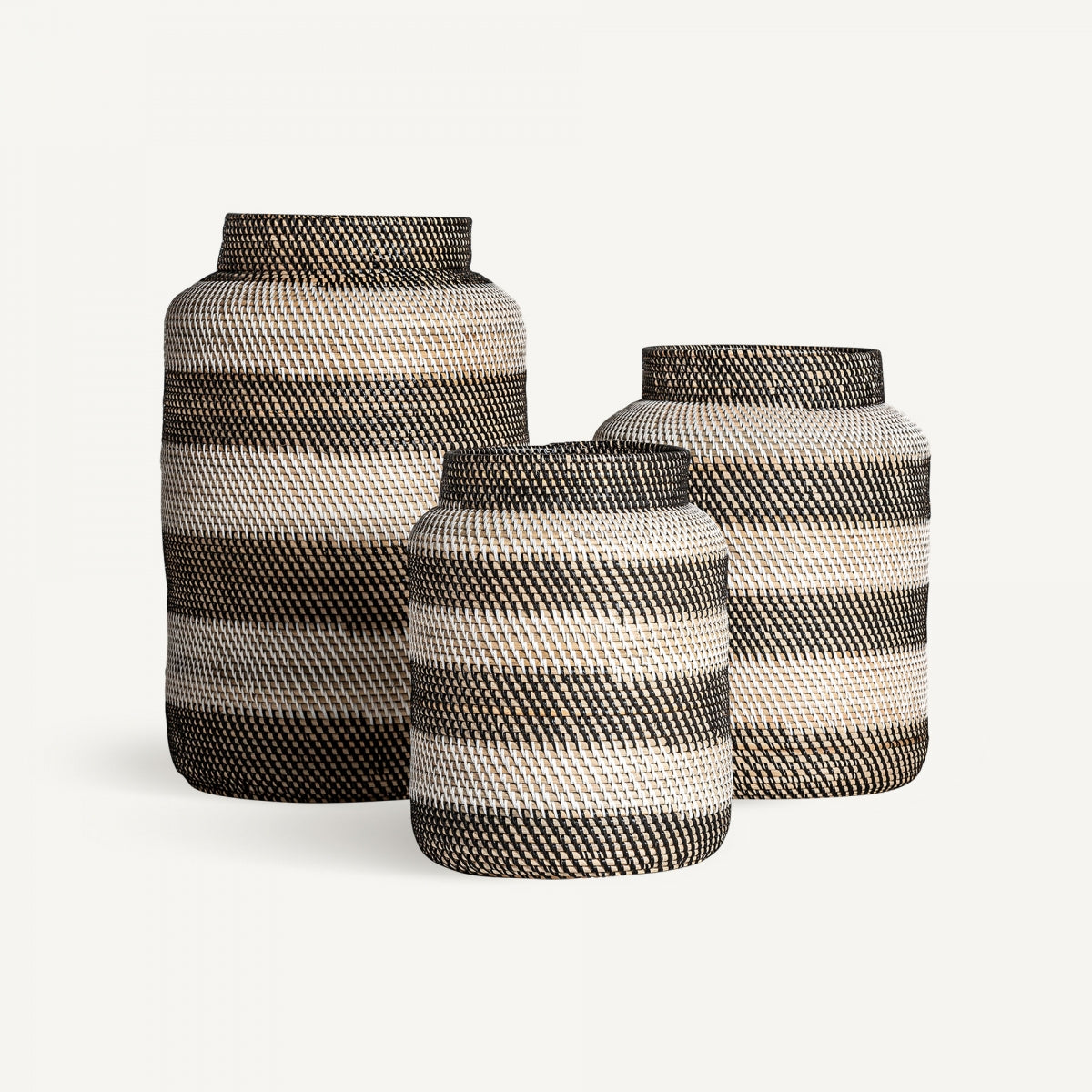Juego de tres jarrones de ratán natural, Jarrón en ratán natural Zirba (3 Piezas), con diseño étnico y anchas rayas horizontales blancas y negras, dispuestas en altura descendente sobre un fondo blanco liso.