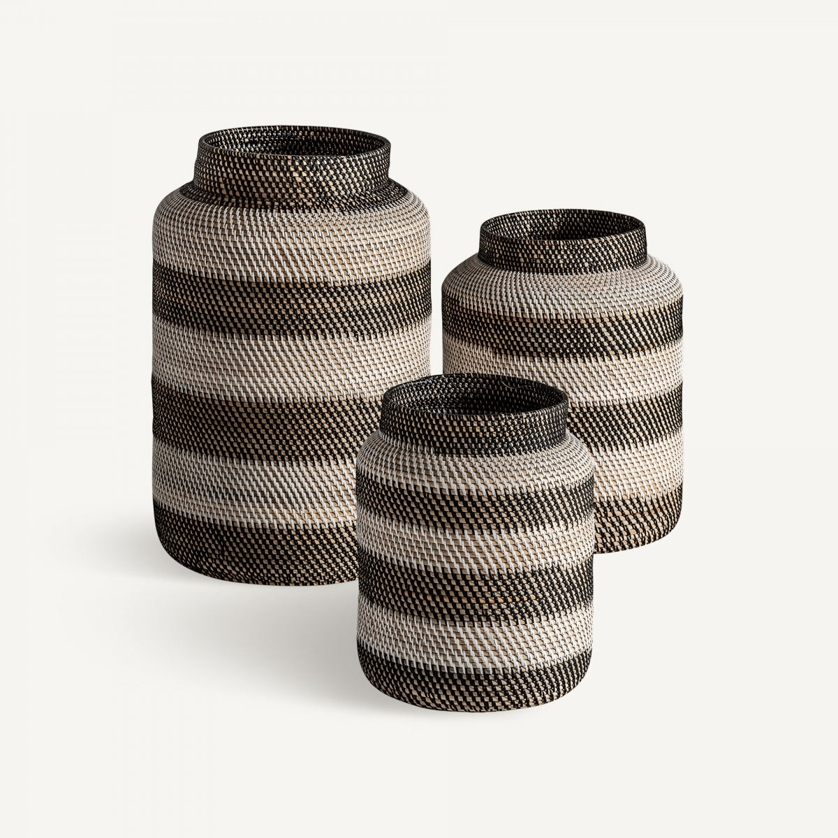 El set Jarrón en ratán natural Zirba (3 Piezas) presenta tres jarrones de distintos tamaños con franjas horizontales en negro, blanco y tonos naturales, que destacan las texturas de ratán y un diseño étnico sobre fondo blanco.