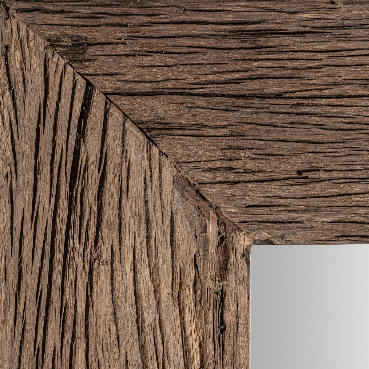Primer plano de una esquina de marco de fotos de madera de pino reciclado, texturizada y resistente, con una vista parcial del Espejo cuadrado de madera reciclada (150x150 cm) Samsun Q en el interior. Ideal para decoración sostenible y étnica.