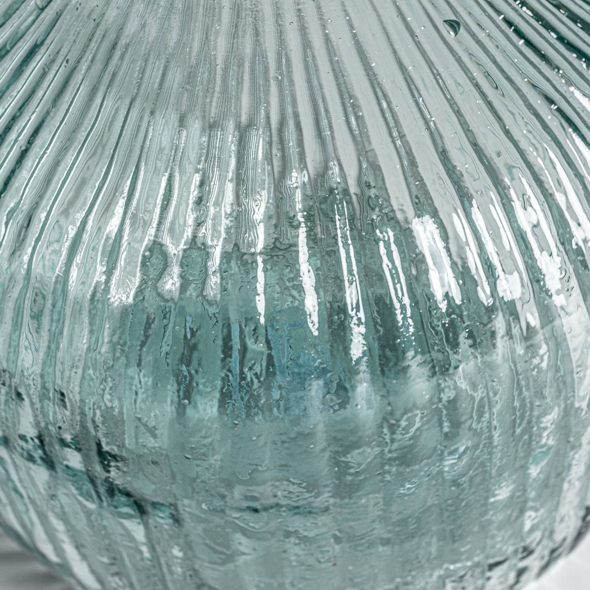 Primer plano del Jarrón en vidrio reciclado El vidrio transparente texturizado con crestas verticales y reflejos de Sumaya A, un detalle elegante para cualquier decoración del hogar.