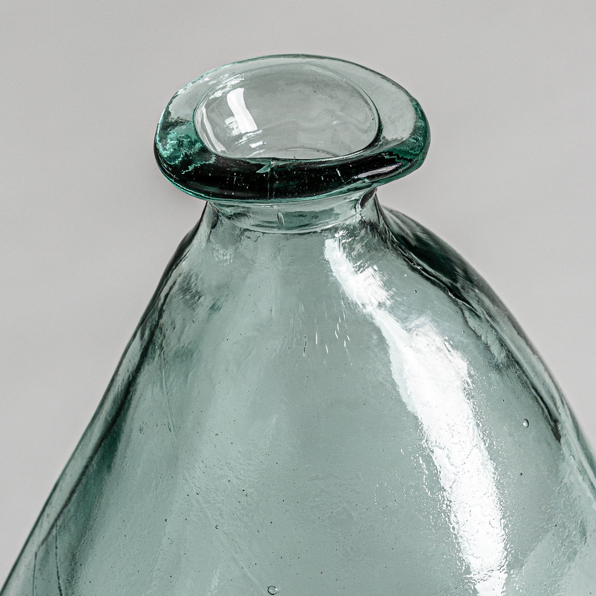 Primer plano del cuello y el borde de un jarrón de vidrio reciclado Sumaya W teñido de verde con un labio ancho y plano sobre un fondo neutro: un ejemplo perfecto de diseño sostenible.