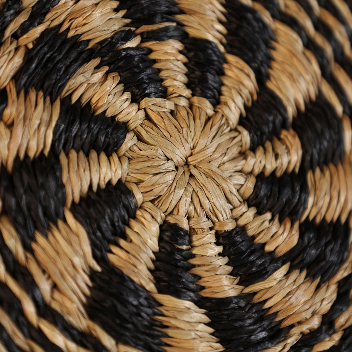 Primer plano del Panel decorativo en rafia Boho Iris, que muestra un patrón en espiral en fibras de rafia naturales en beige y negro, ideal para agregar encanto boho a cualquier espacio.