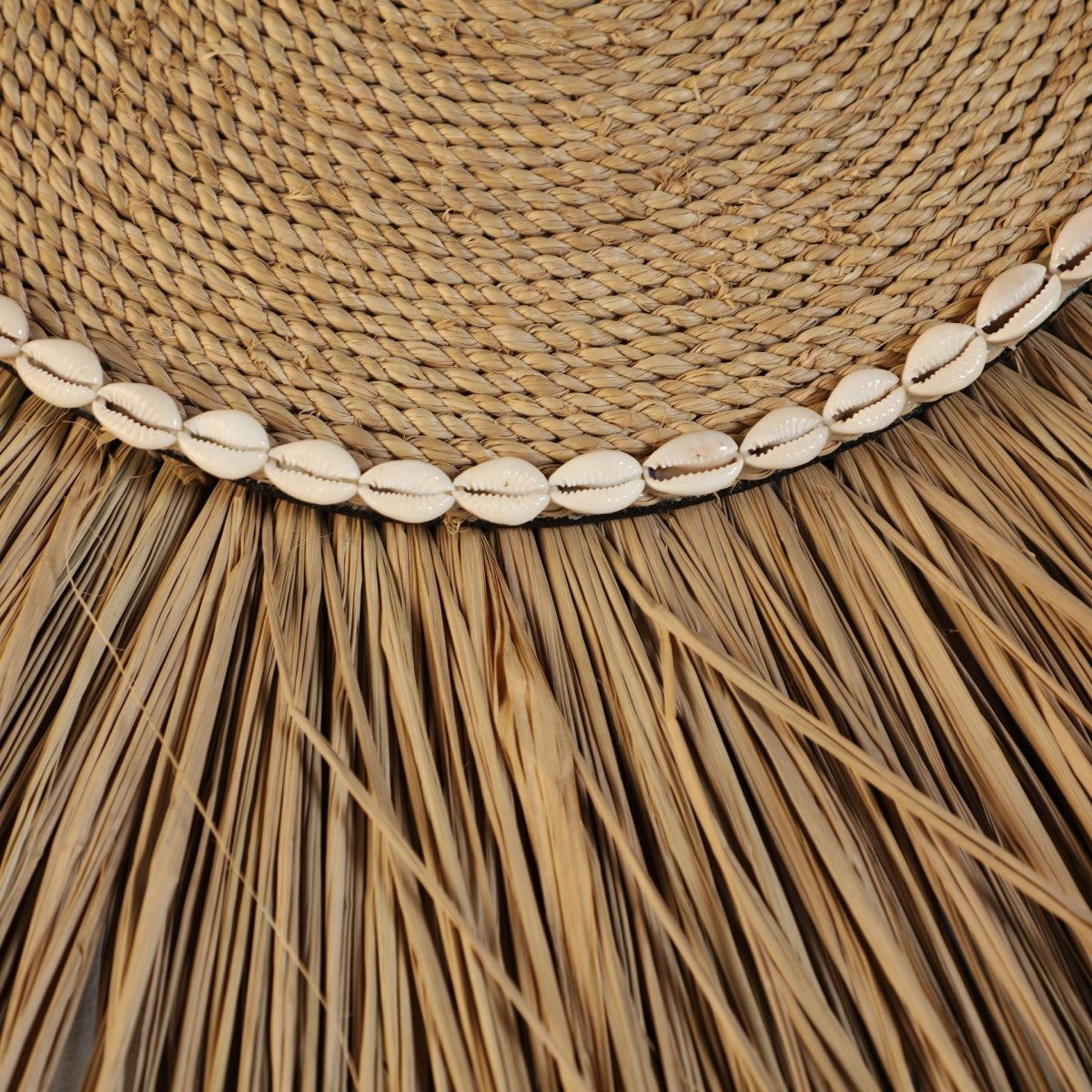 Primer plano del Panel decorativo en rafia marrón Boho, con paja tejida bordeada con conchas de cauri y fibras de rafia marrón, ideal para agregar un toque boho chic a su interior.