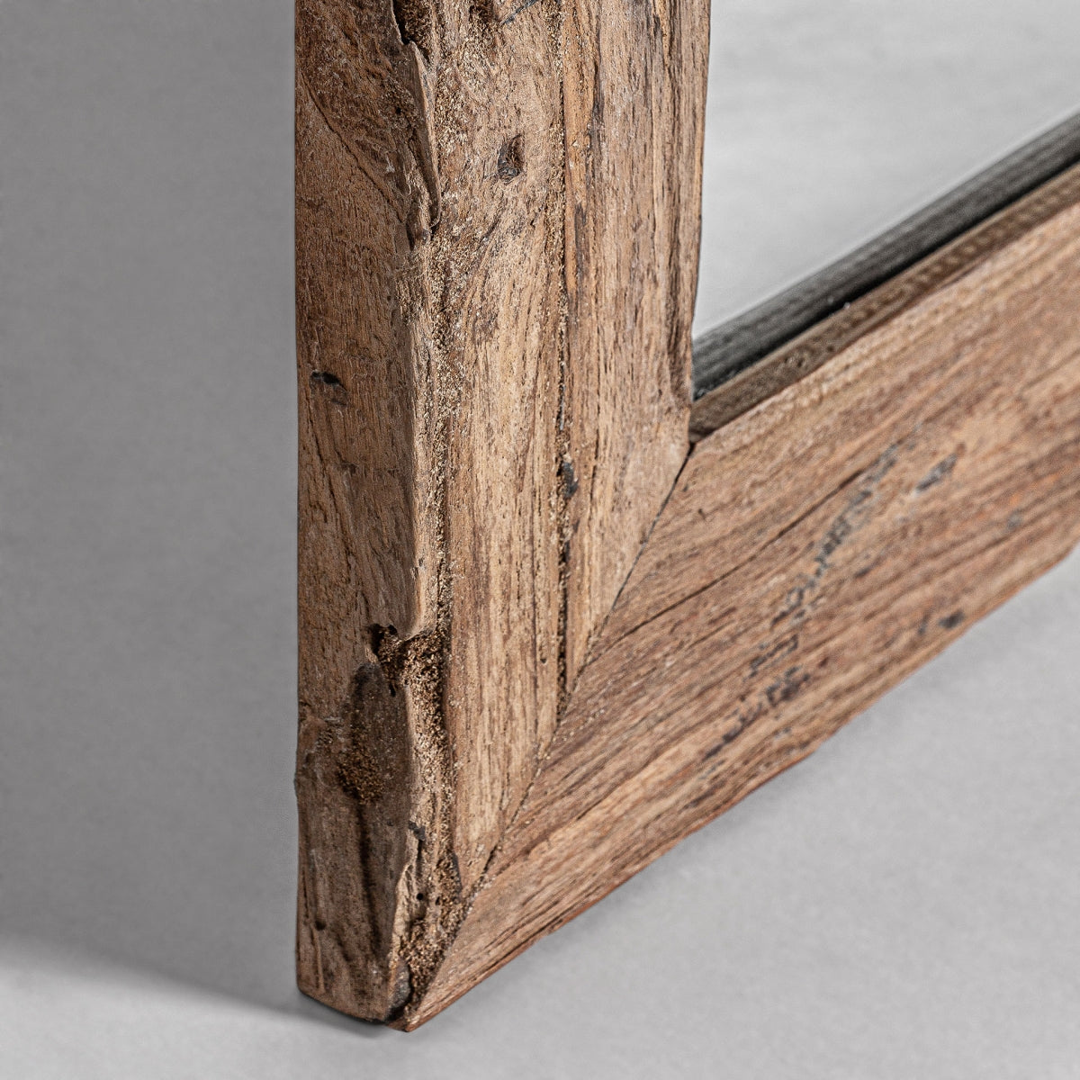 Primer plano de una esquina del Espejo de pared en madera de teka (65x150 cm) Lux S, que muestra la veta visible de la madera de teca, juntas ingleteadas y un toque de diseño colonial sobre un fondo gris claro.