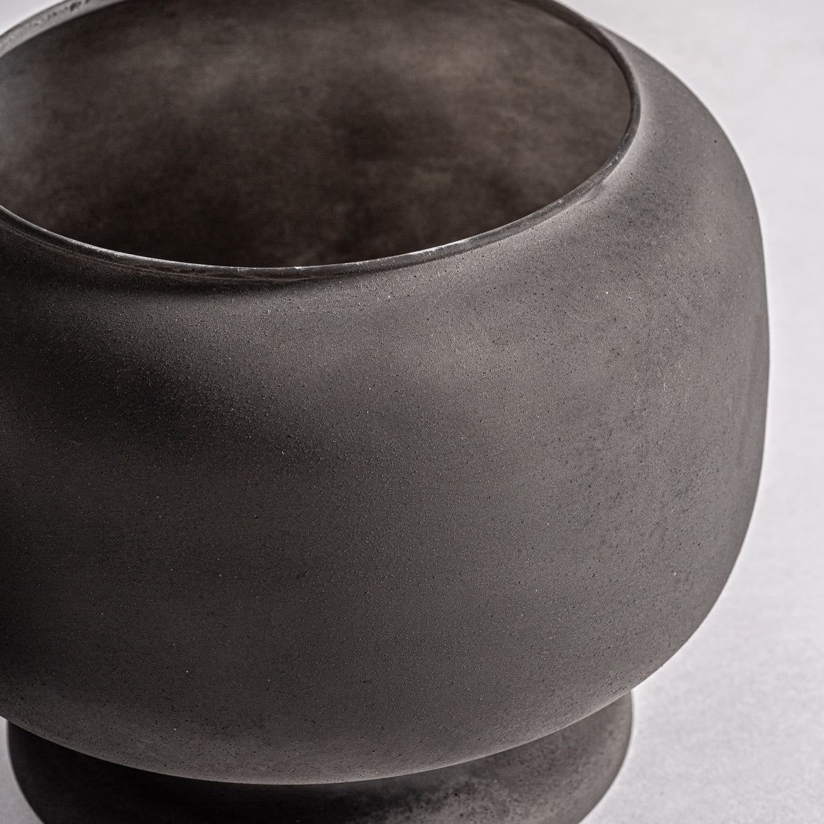Jarrón contemporáneo en vidrio negro envejecido Blaj, de forma redondeada y boca ancha, combina elegancia y modernidad sobre un fondo gris claro.
