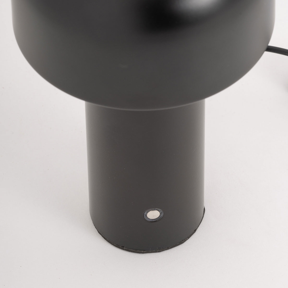 Primer plano de la base de la Lámpara de sobremesa en hierro negro Malik, que presenta un pequeño botón circular cerca de la parte inferior, sobre un fondo blanco liso y que refleja un estilo de diseño Art Deco.