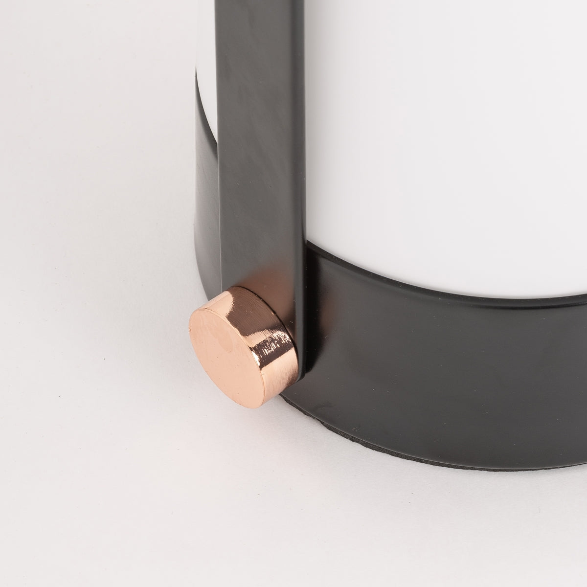 Primer plano de la lámpara de mesa de hierro y cristal Kaila, que muestra su marco negro, cuerpo de vidrio blanco en forma de cúpula y acento de base circular de color cobre.