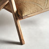 Primer plano de la pata y la tela tejida del asiento del Sillón de madera y yute Elgin sobre una superficie clara. El acabado de madera natural y la tela con sutiles estampados evocan un ambiente rústico, evocando el encanto atemporal del diseño vintage.