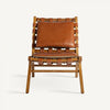 El sillón en piel y madera de fresno Alford presenta un respaldo y un asiento con correas de cuero tejido combinados con un cojín de cuero marrón sobre un marco de madera clara, evocando un estilo art déco.