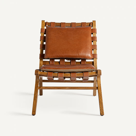 El sillón en piel y madera de fresno Alford presenta un respaldo y un asiento con correas de cuero tejido combinados con un cojín de cuero marrón sobre un marco de madera clara, evocando un estilo art déco.